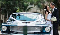 Front View Blue Shelby 1965 Mustang Fastback with newly-weds holding the bride’s bouquet