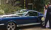 Side view Blue Shelby 1965 Mustang Fastback with newly-weds holding a flower bouquet