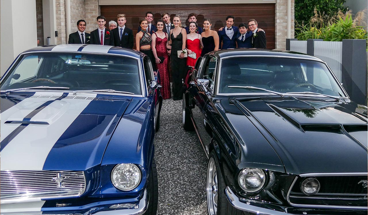 Front view Blue Shelby 1965 Mustang Fastback and young attractive couple in formal attire